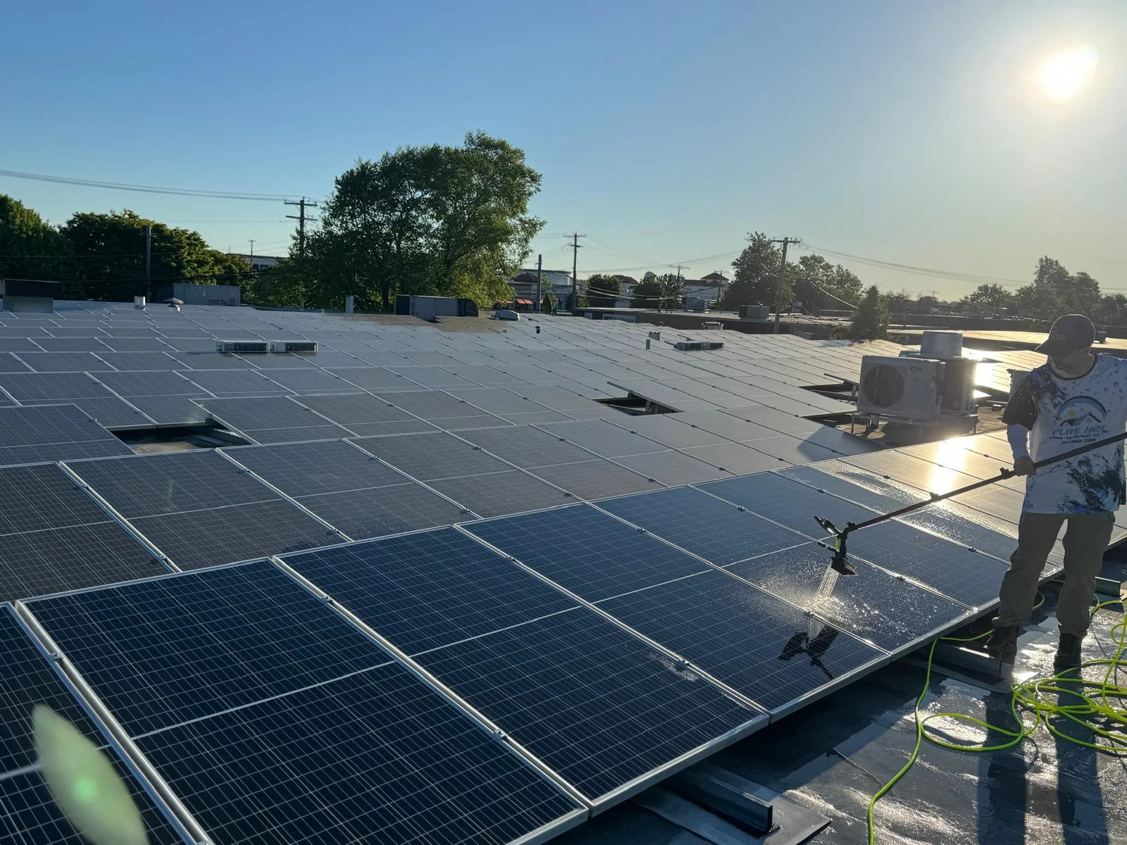 Wide view of technician washing rooftop commercial solar panel array